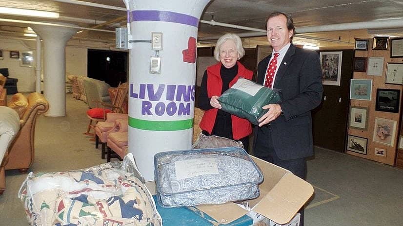 Bill O'Donnell and a woman stand with multiple donated blankets and bedspreads.