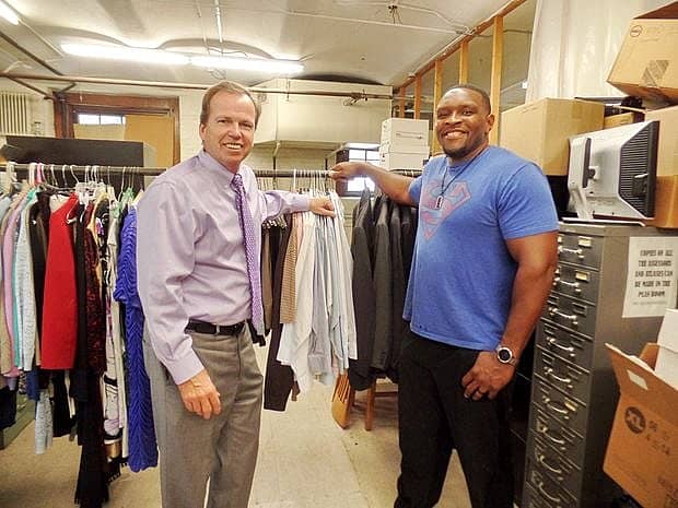 Bill O'Donnell stands with another man in front of a rack of clothes.